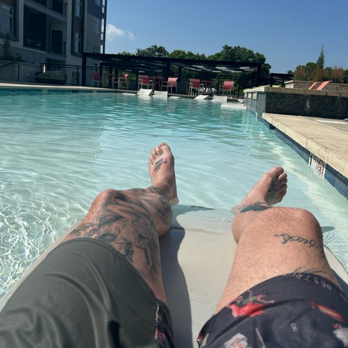 A person relaxes on a pool ledge at a rooftop pool, with tattooed legs extended into the clear water and a poolside lounge area visible in the background. The scene captures a laid-back summer vibe, fitting the "Happy Solana Summer" caption with its sunny, leisure-focused atmosphere.