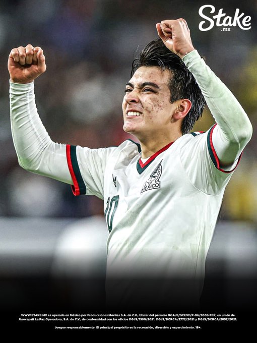 A soccer player wearing a white Mexico national team jersey with the number 10 celebrates with raised fists, with a 'Stake.mx' logo in the corner.