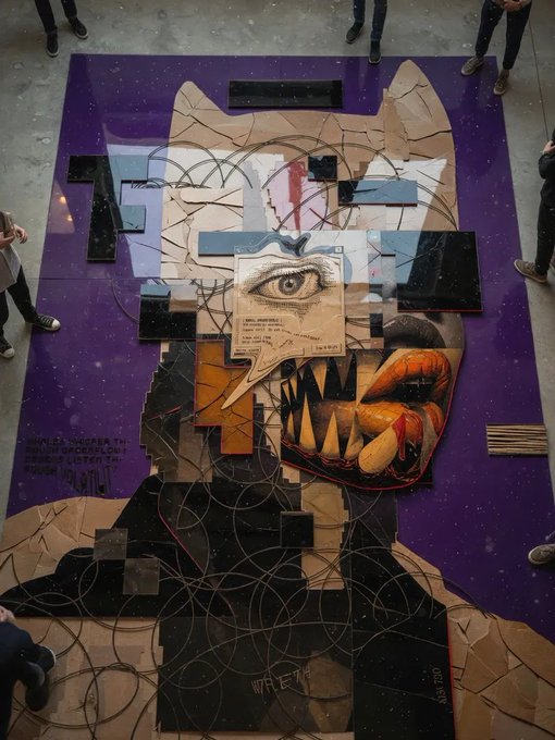 A large floor-based mixed-media artwork featuring a fragmented face with an eye, teeth, and orange lips on a purple background, viewed from above with people's feet visible around the edges.