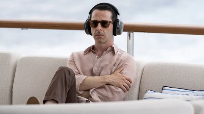 A man wearing sunglasses and headphones sits with crossed arms on a cream-colored outdoor sofa, exuding a cool, unbothered demeanor—visually embodying the casual, confident "done" tone of the post about reaching the $50M milestone.