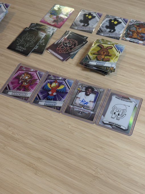 Trading cards scattered on a wooden table, featuring characters including 'Werewolf,' 'Parrot,' 'USA,' and a sheep, with stacks of additional cards visible in the background.