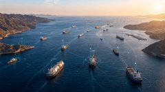 An aerial view shows numerous large cargo ships anchored in a sunlit coastal harbor, illustrating the dense maritime traffic that the accompanying post describes as difficult to monitor reliably. The image visually emphasizes the challenge of vessel tracking, which the post attributes to AIS vulnerabilities and the need for verification tools like gETHRA's service.