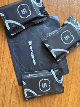 Several black Unruggable-branded packets with a white 'W' logo are scattered on a wooden table, resembling condom or supplement packaging.