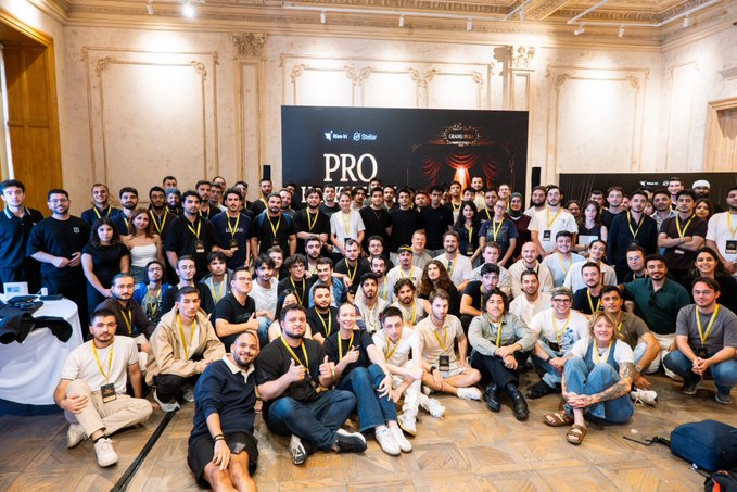 A large group photo of attendees at a Binance event, gathered in front of a backdrop displaying 'Binance' and 'PRO' logos.