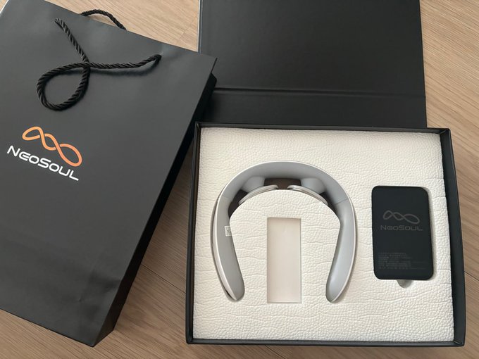 A black NeoSOUL branded shopping bag next to an open product box displaying a pair of white wireless neckband headphones and a small black accessory on a wooden surface.