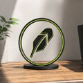 A decorative round artwork featuring a green leaf design on a black background sits on a wooden surface in a minimalist setting.