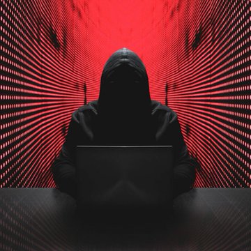A hooded figure sits in front of a laptop in a dimly lit room with red LED-lined walls, suggesting a hacker or cyber-themed scene.