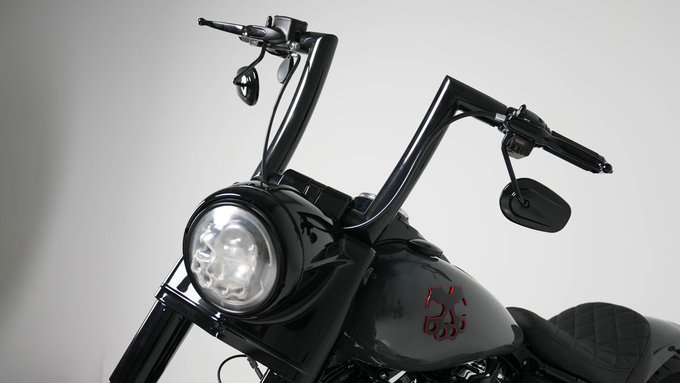 A close-up view of a black motorcycle features tall handlebars, a round LED headlight, and a glossy fuel tank marked with a red "88" decal.