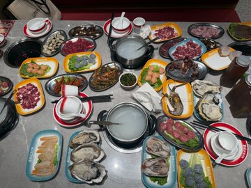 A table is filled with an elaborate hot pot feast featuring numerous plates of raw meats, seafood, vegetables, and dipping sauces arranged around two simmering pots of broth, set for a communal meal.

The image contrasts sharply with the post's tutorial text, which humorously outlines steps for "fleece-raking" at Hoshino University and dealing with "Little Hu @MetaJohnWick," highlighting an ironic disconnect between the hearty dining scene and the scheming financial advice described.