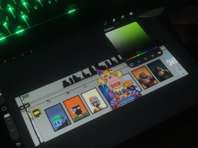 A tablet displays a pixel art game or application with various character sprites, a color picker, and a cityscape silhouette, resting next to a green backlit keyboard.