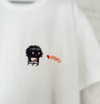 A close-up of a white t-shirt featuring a small cartoon illustration of a fluffy black character next to a red heart.