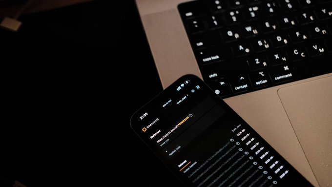 A smartphone displaying a stock market watchlist app with entries for "BTC/USD" and "ETH/USD" rests on a MacBook laptop keyboard, illustrating the convenience of multi-asset trading mentioned in the post about @TrueCurrentX.