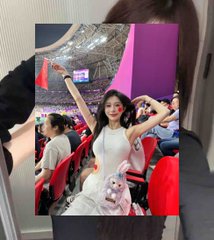 A photo being held up showing a smiling woman in a white dress at what appears to be a concert or event, making hand gestures toward the camera.