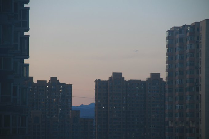 A dusk view of a city skyline featuring silhouetted high-rise apartment buildings against a gradient sky of blue and pink, with a mountain visible in the distance.