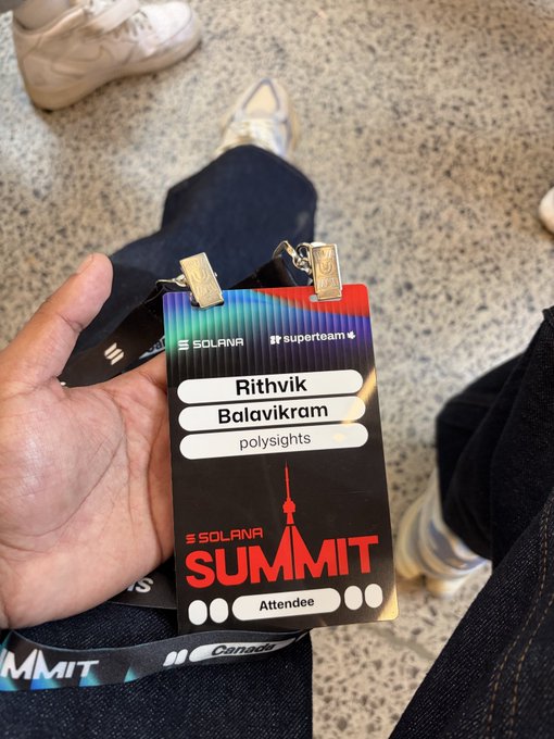 A hand holds a Solana Summit attendee badge for 'Rithvik Balavikram' from 'polysights', with a Solana logo and red summit graphic.