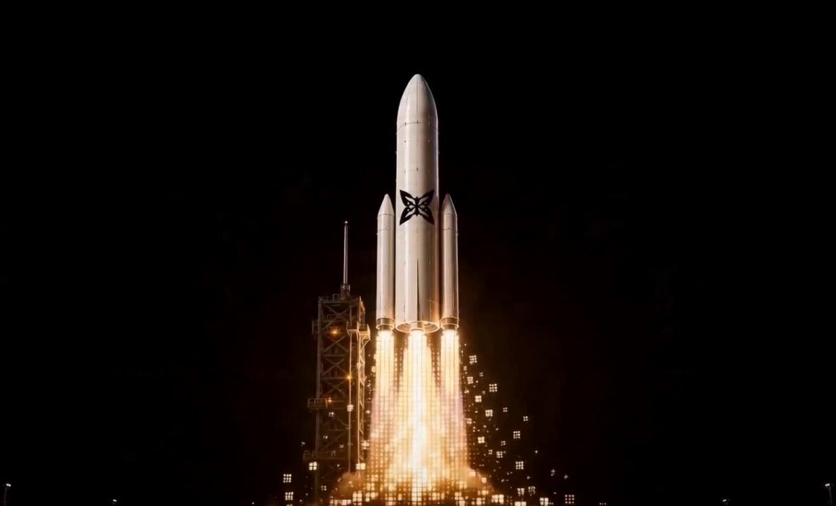 The image features an impressive rocket launch taking place at night. The rocket is white and black with a large X symbol on its side, indicating that it's a space shuttle or a satellite. It's launching into space from a launchpad, which can be seen in the background of the photo. The sky around the rocket is dark, emphasizing the brightness of the rocket as it soars through the air.