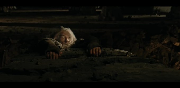 A cinematic shot of a white-haired, bearded man (resembling Rick from Rick and Morty) clinging to a ledge in a dark, rocky environment.