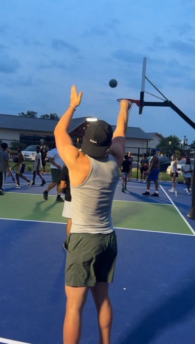 A person in a gray tank top and black cap shoots a basketball on an outdoor court, capturing the moment the ball leaves their fingertips toward the hoop. The caption "$GIGA Swish." cleverly connects to the photo by implying a perfectly made shot, with "swish" being basketball slang for a clean shot that goes through the net without touching the rim.