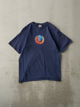 A navy blue short-sleeved t-shirt laid flat on a gray surface, featuring a small circular graphic on the chest that appears to depict a globe or earth design.
