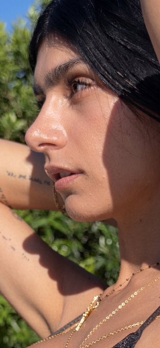 The image features a woman with long dark hair wearing a black top, who has tattoos on her arm. She is looking off into the distance while holding onto a piece of paper or a card attached to her shirt. The text "can i get a GM?? @useTria x @TheARCTERMINAL x @quipnetwork and @wallchain are on my radar now" can be seen in the image, which suggests that she is interested in receiving messages from someone named "@useTria".