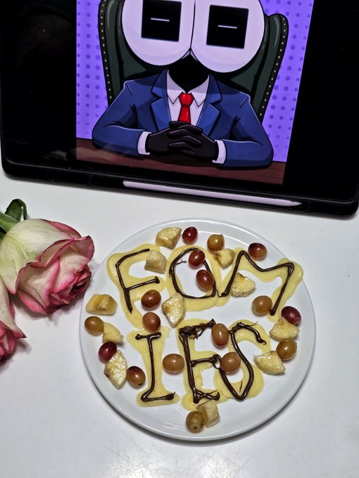 A breakfast plate with eggs, grapes, and sauce spelling 'FÒ́V IHF' beside a rose and a tablet displaying a cartoon character in a blue suit with a TV-like head.