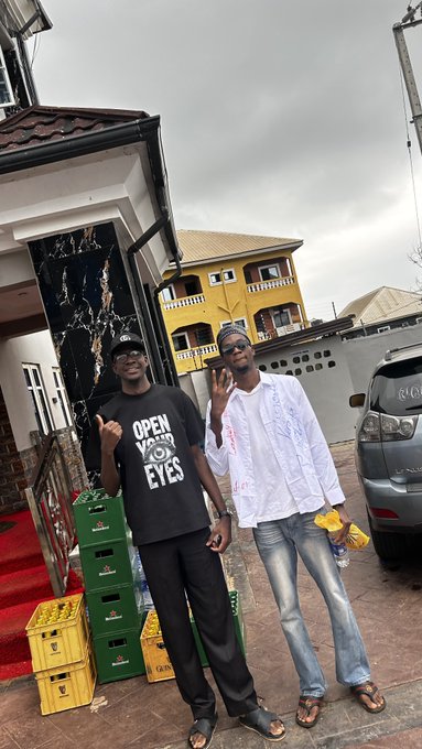 Two men pose together outside a yellow building, one wearing a black "OPEN YOUR EYES" t-shirt and the other in a white textured shirt and sunglasses, with stacked green and yellow beverage crates at their feet—fitting the casual "More jpegs" caption with a relaxed, candid vibe.