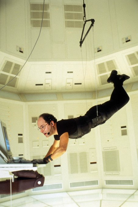 A man wearing a headset and tactical gear appears to be floating horizontally in a zero-gravity environment, typing on a keyboard attached to a workstation.