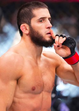 A shirtless UFC fighter with a beard raises a black glove to his face in the octagon, reflecting on a confident victory. The image relates to the post about a bettor wagering $187,000 on Polymarket that Islam Makhachev would beat Ian Garry, with Makhachev extending his unbeaten streak to 17 consecutive UFC victories.