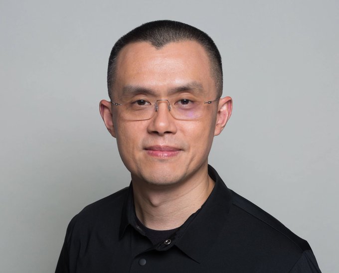 A man wearing a black polo shirt and rimless glasses poses for a portrait against a plain gray background, with a faint bruise visible near his left eye. The image corresponds to CZ (Changpeng Zhao), the former CEO of Binance, whose vision for tokenized on-chain IPOs aligns with the post's discussion of transforming public capital markets through blockchain technology.