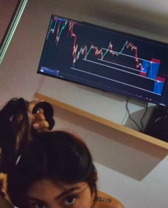 A trader with headphones is intensely focused on a large monitor displaying a candlestick chart with a sharp downtrend, capturing the "locked in on the charts" vibe of the post.