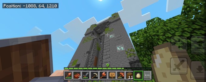 A first-person perspective screenshot from the video game Minecraft, showing the player holding a block and looking up at a tall stone tower with vines, with their inventory hotbar visible at the bottom and coordinates '-1088, 64, 1210' in the top left.