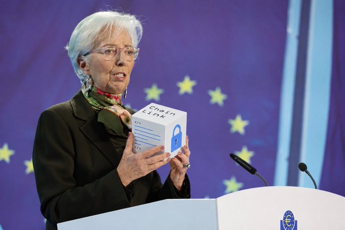 Christine Lagarde holds up a white cube labeled 'Chain Link' with a padlock icon while speaking at an EU podium.
