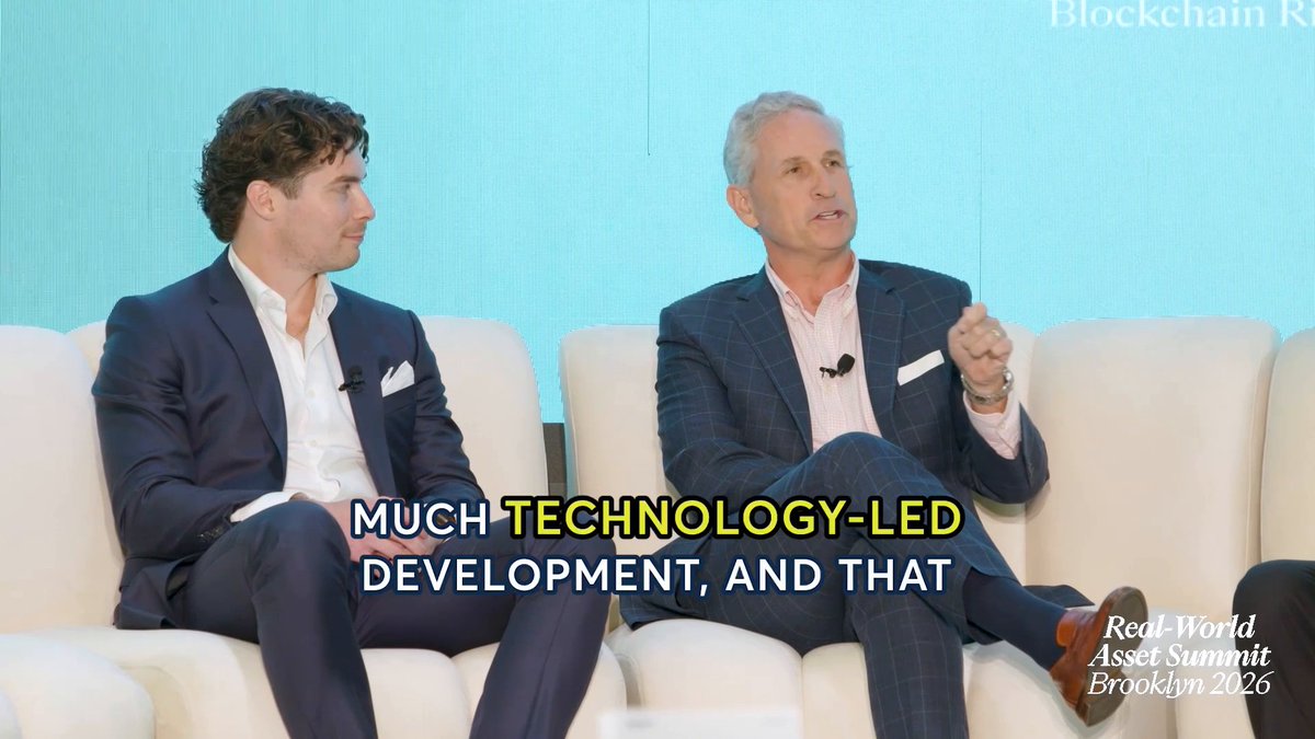 Two men sit on white chairs on a stage at the Real-World Asset Summit Brooklyn 2026, with on-screen text reading "MUCH TECHNOLOGY-LED DEVELOPMENT, AND THAT," as the speaker on the right, likely Derek from CME Group, gestures while discussing tokenization's role in the future of markets alongside a younger panelist listening attentively.