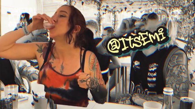 A stylized, heavily filtered photo showing a tattooed woman in an orange top drinking from a shot glass alongside a tattooed man, with the text '@ItsEmi' overlaid on the image.
