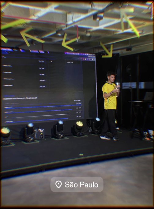 A person in a yellow shirt stands on a stage with a large display screen, located in São Paulo as indicated by a location tag overlay.
