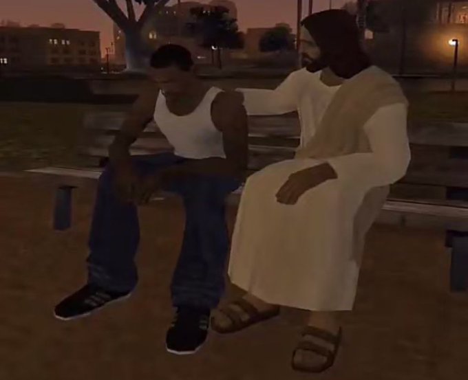 A low-resolution screenshot from a video game (likely GTA San Andreas) showing a young Black man in a white tank top and blue jeans sitting on a park bench next to a bearded man in a white robe.
