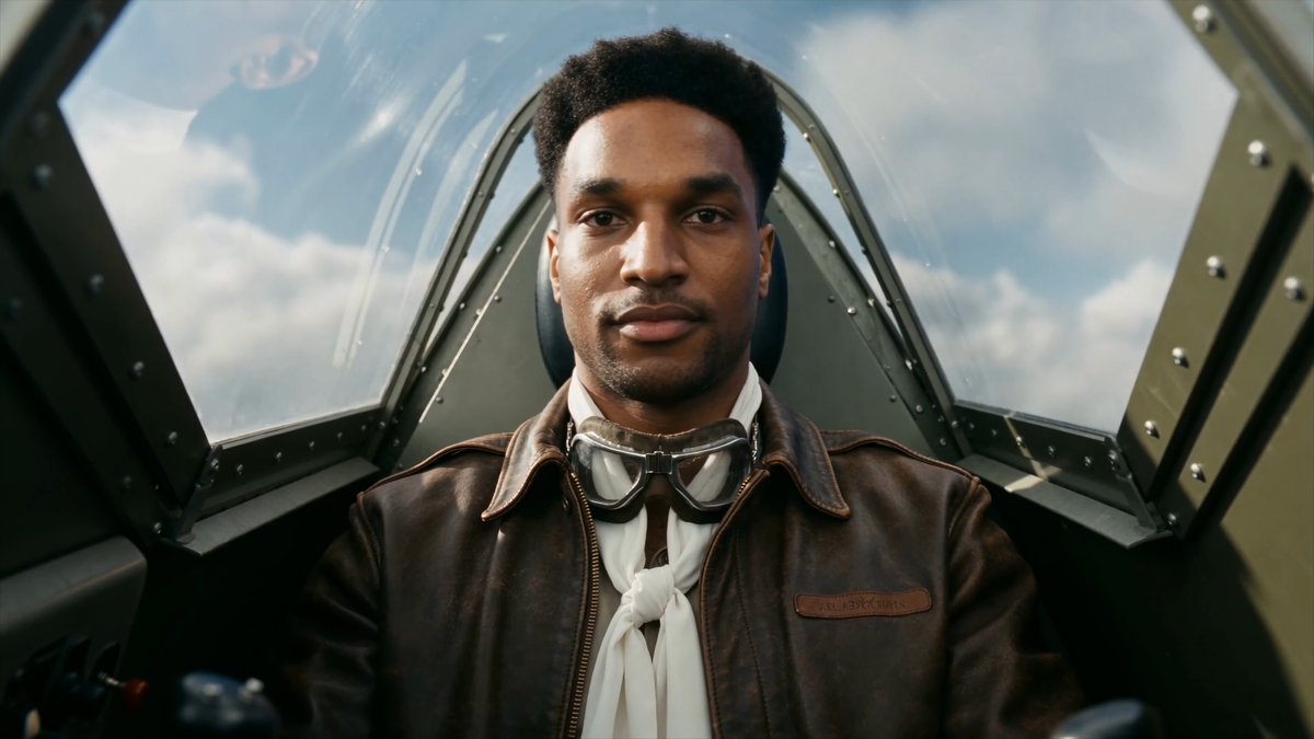 A young Black pilot in a vintage aircraft cockpit wears a brown leather "Tuskegee" flight jacket with goggles around his neck, evoking the historic WWII Tuskegee Airmen. The image reimagines ANSEM as a heroic pilot, fitting the cinematic "ANSEM: The Movie (based on a true story)" theme tied to the $ANSEM token.