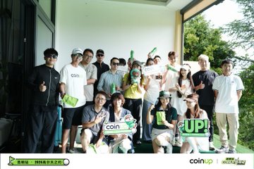 The image shows a group of people posing for a photo at a golf course. They are all holding up signs that say "coinup" or "Up", indicating their support for the coinup travel company. The group consists of both men and women, with some standing in front of a building while others are on the golf course itself. There is also a chair visible near the left side of the image.