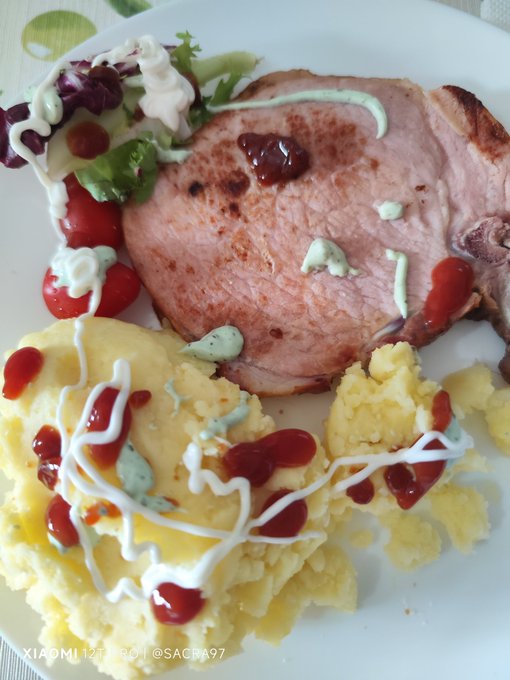 A plate of food, including mashed potatoes covered with ketchup sauce and a cooked piece of meat alongside other food items such as tomatoes and lettuce.
