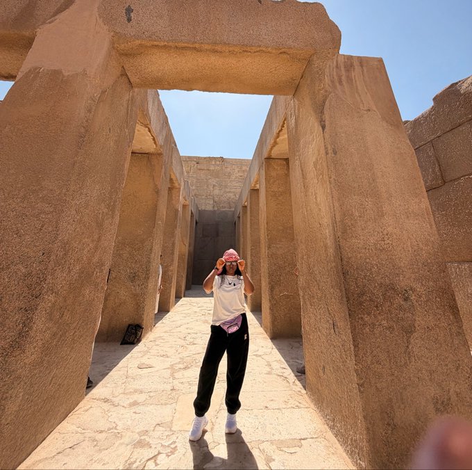 A person in a bucket hat poses between massive stone pillars at an ancient Egyptian site, capturing a moment of travel and adventure. The image reflects the post's prompt about future hopes, suggesting the dream of exploring iconic historical landmarks around the world.
