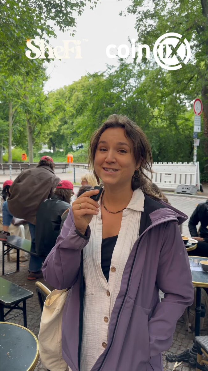 The image features a woman wearing a purple jacket, standing outside with her hand over her mouth as if she's about to speak or make a funny face. She has a bag next to her and appears to be posing for a photo. The background of the image shows trees and other people in the area, suggesting that they are at an outdoor gathering or event. There is also text present in the image, which reads "We had access to @base before it was available to the public. wanna know why? Because we're SheFiers! Being part of the @shefiorg community comes with incredible advantages. A special thank you to @solana for sponsoring the new cohort. @BerBlockWeek @maggielove_ @SuperteamDE".