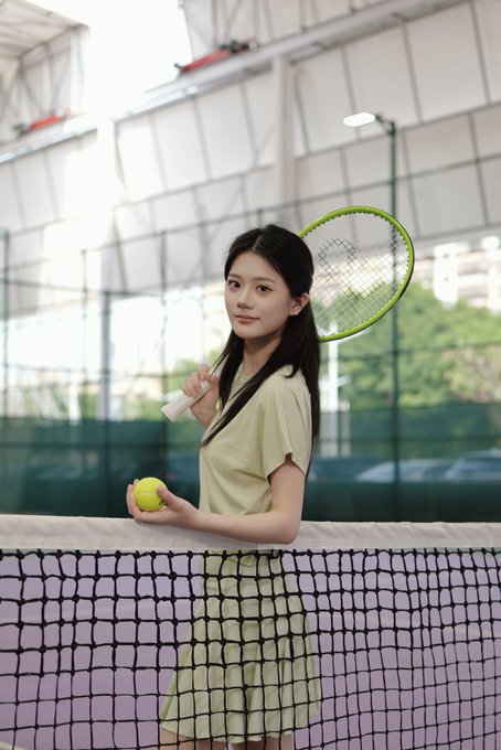 A young woman in a light green dress stands behind a tennis net, holding a tennis racket over her shoulder and a tennis ball in her hand.

The image ties to the post by visually representing the "ultra-premium physical tennis racket giveaway," showing the kind of tennis-themed lifestyle and elegance being offered as a prize alongside the Panda Welfare trading giveaway.