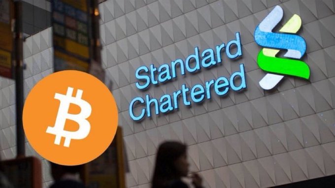 In this image, a woman wearing a black shirt is standing next to an advertisement for Standard Chartered bank on a building. The logo for Bitcoin is displayed above her. It appears that there may be some connection or discussion between these two elements within the context of the image and the posted message. However, it is not possible to determine with certainty what this connection might be in relation to the image's content or the message itself.