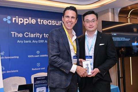 Two men pose together at a Ripple Treasury event in Hong Kong, with one presenting a small gift or award to the other in front of a backdrop promoting "The Clarity to" with benefits including "100% cash visibility" and "Reduce cost."