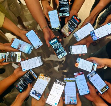 A group of people hold their smartphones in a circle, all screens displaying various social media feeds and messages.