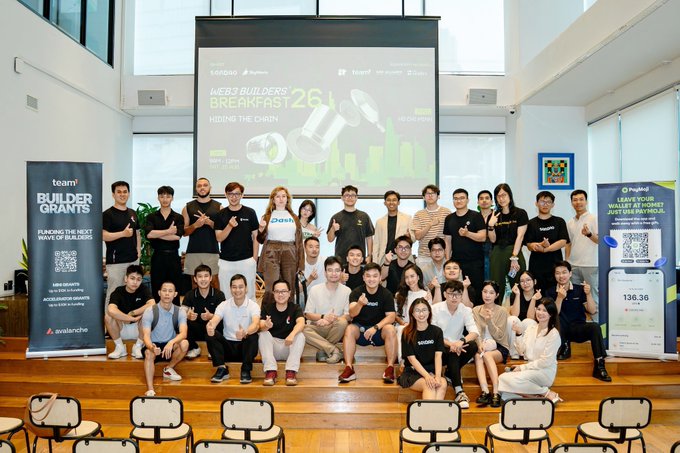 A group photo from the 'Web3 Builders Breakfast 26' event hosted by Saigon, featuring team members in front of banners for 'Builder Grants' and a Web3 wallet giveaway, with logos for Avalanche, Sui, Aptos, and others visible.