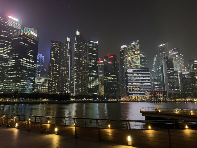 A nighttime skyline view of a modern city waterfront with illuminated skyscrapers reflecting on the water.