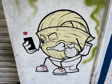 A street art mural of a cartoon egg character wearing bandages, holding a spray paint can with an angry expression.