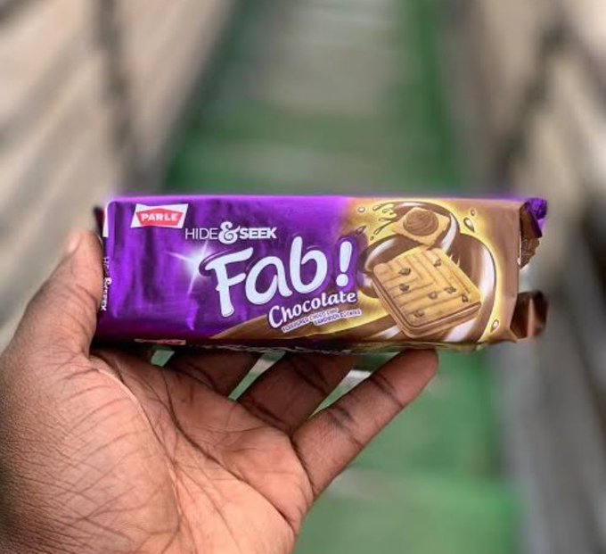 A hand holding a purple wrapper of Parle Hide & Seek Fab! Chocolate biscuits against a blurred background.