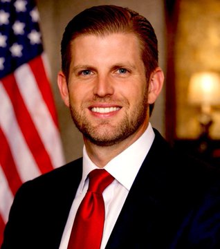 The image shows Eric Trump, wearing a dark suit, white shirt, and red tie, standing in front of an American flag with a warm, smiling expression. This portrait accompanies his bullish statement about Bitcoin, lending a formal and confident tone to his endorsement of the cryptocurrency.